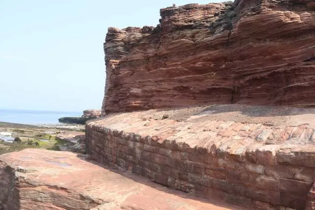 Layered red sandstone cliff beside an old stone wall on Hilbre